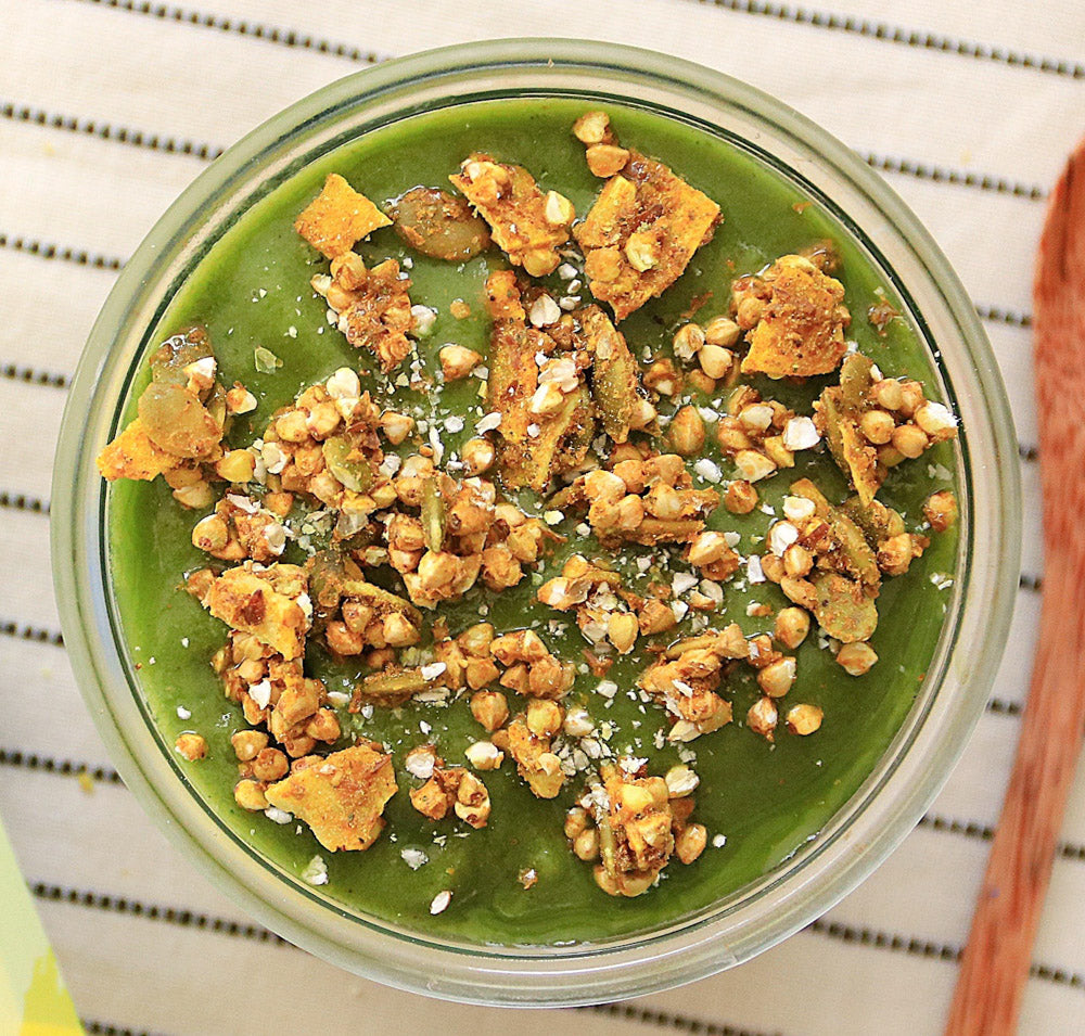 Overhead view of a green smoothie bowl topped with Clusterbucks crunchy granola and seeds on a striped cloth background