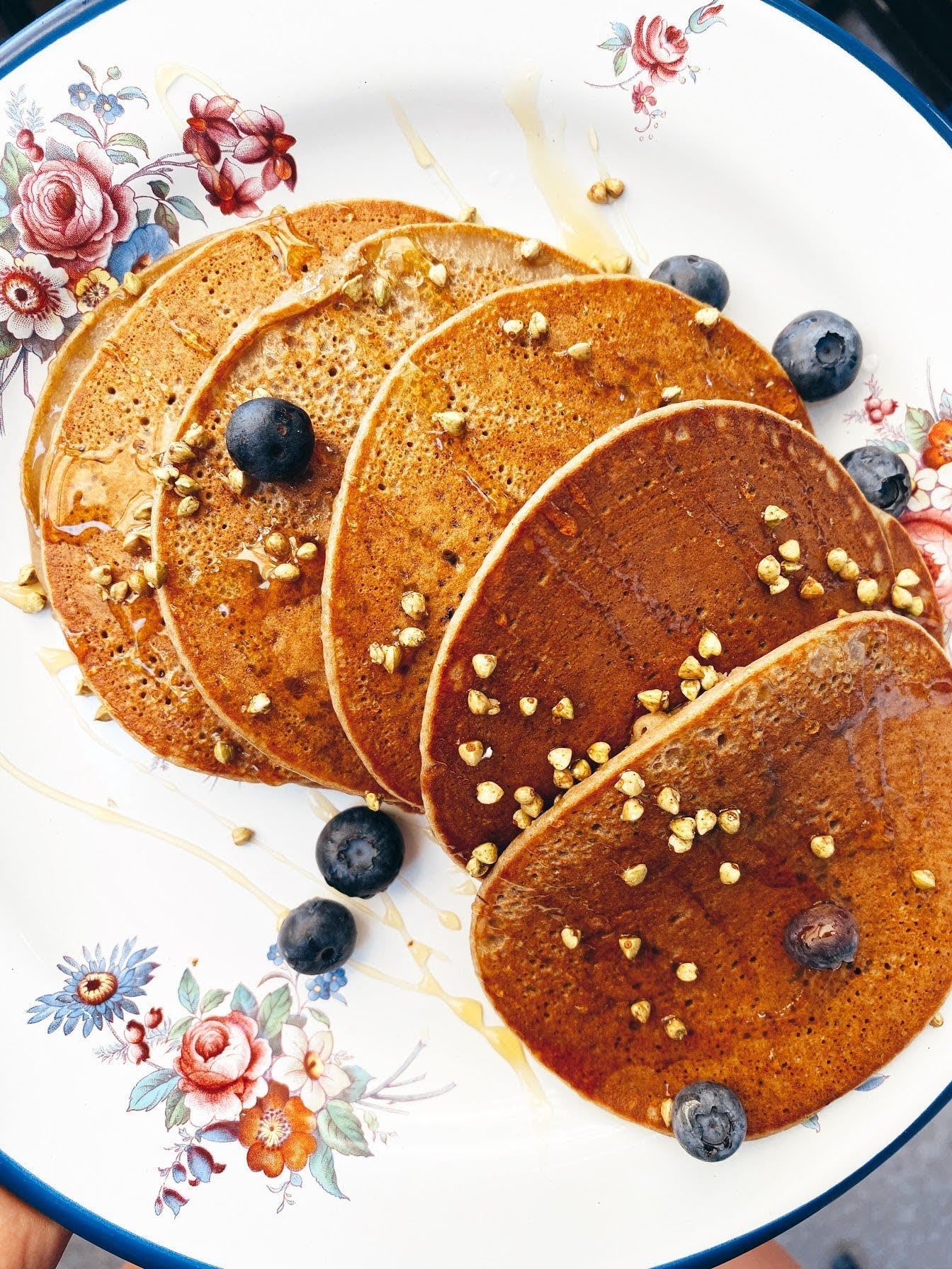 Overhead view of sprouted buckwheat pancakes topped with toasted buckwheat groats, blueberries and honey on a floral plate