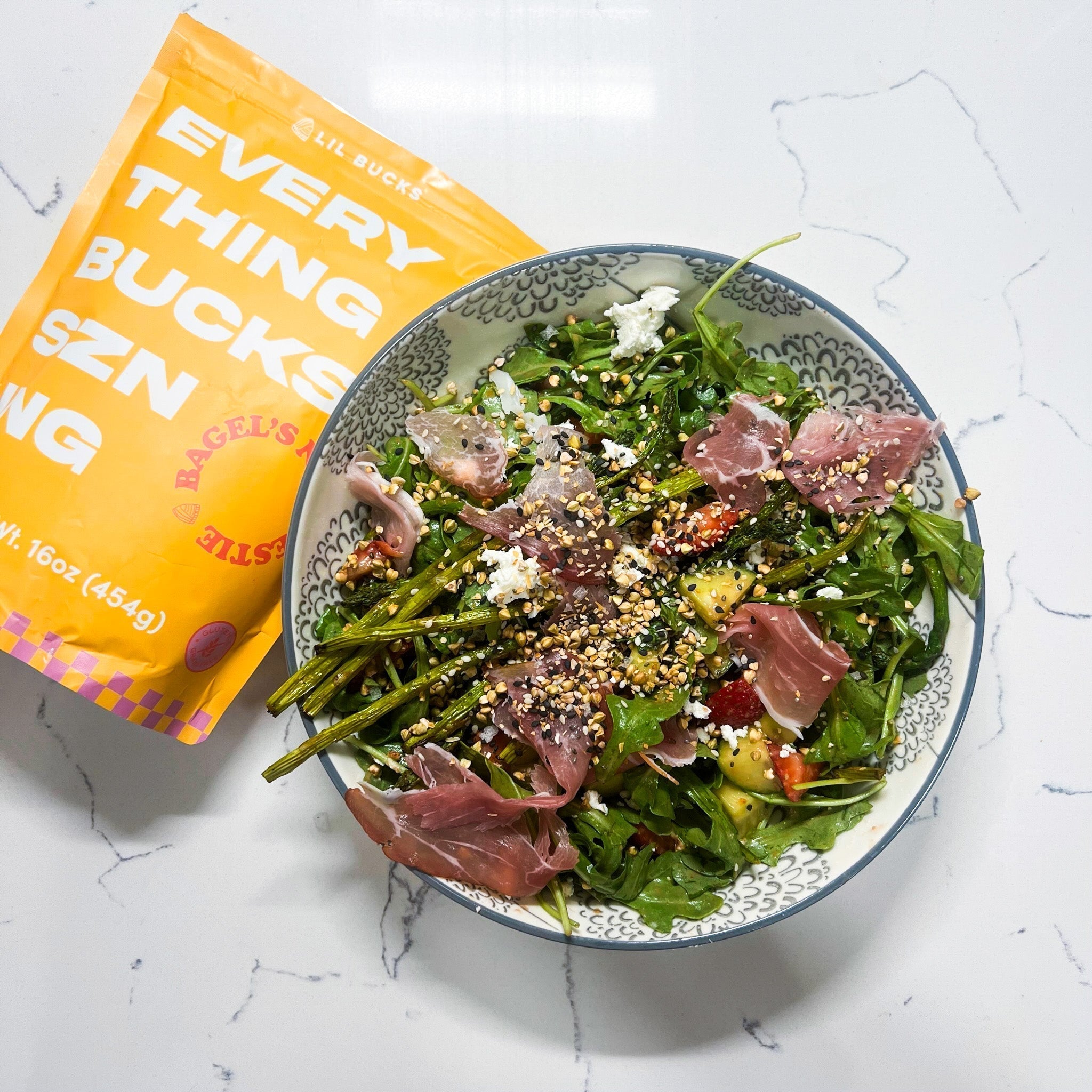 Arugula salad with prosciutto, avocado and asparagus, sprinkled with Everything Bucks seasoning, product bag visible