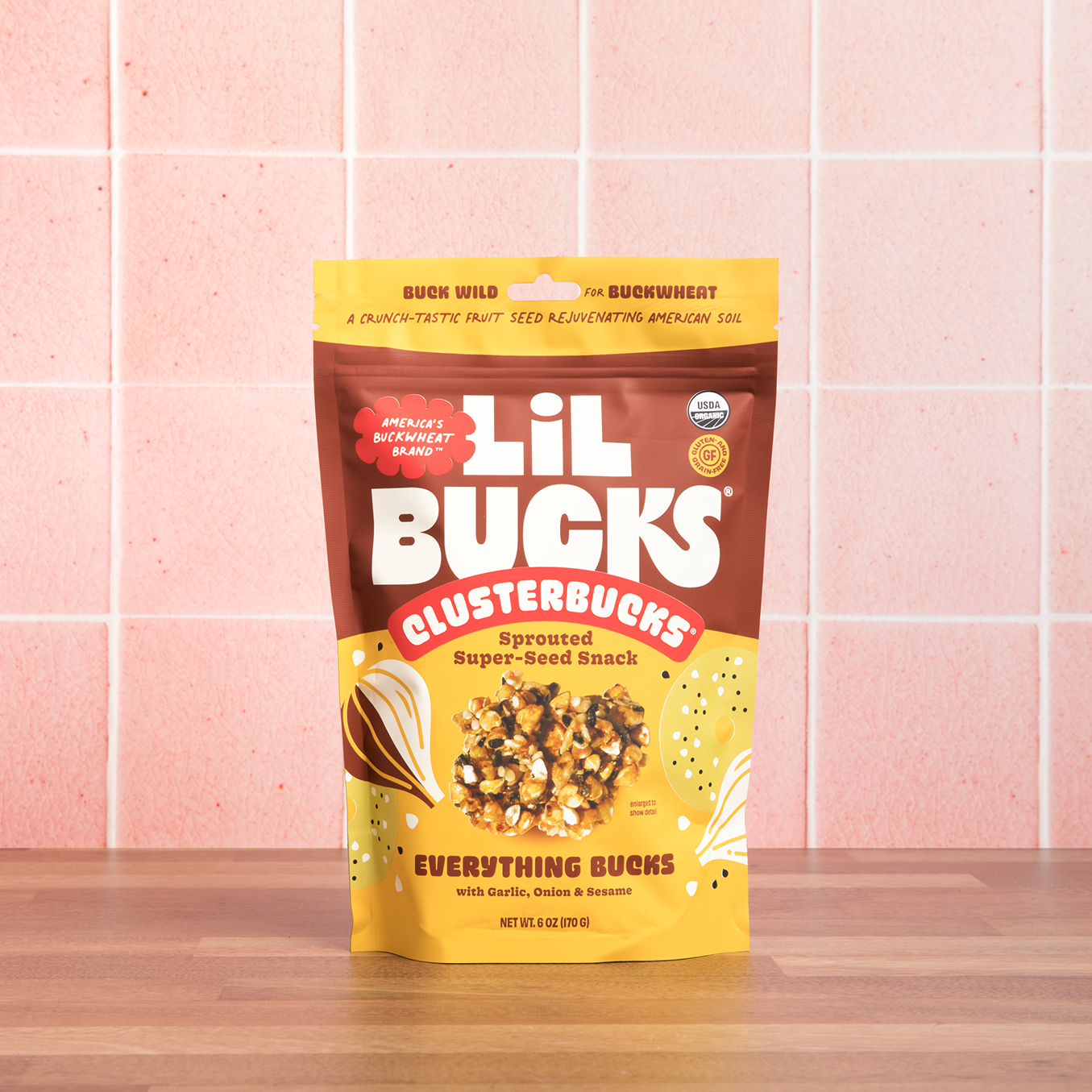 Lil Bucks Clustebucks snack package on a wooden surface with a pink tiled wall background
