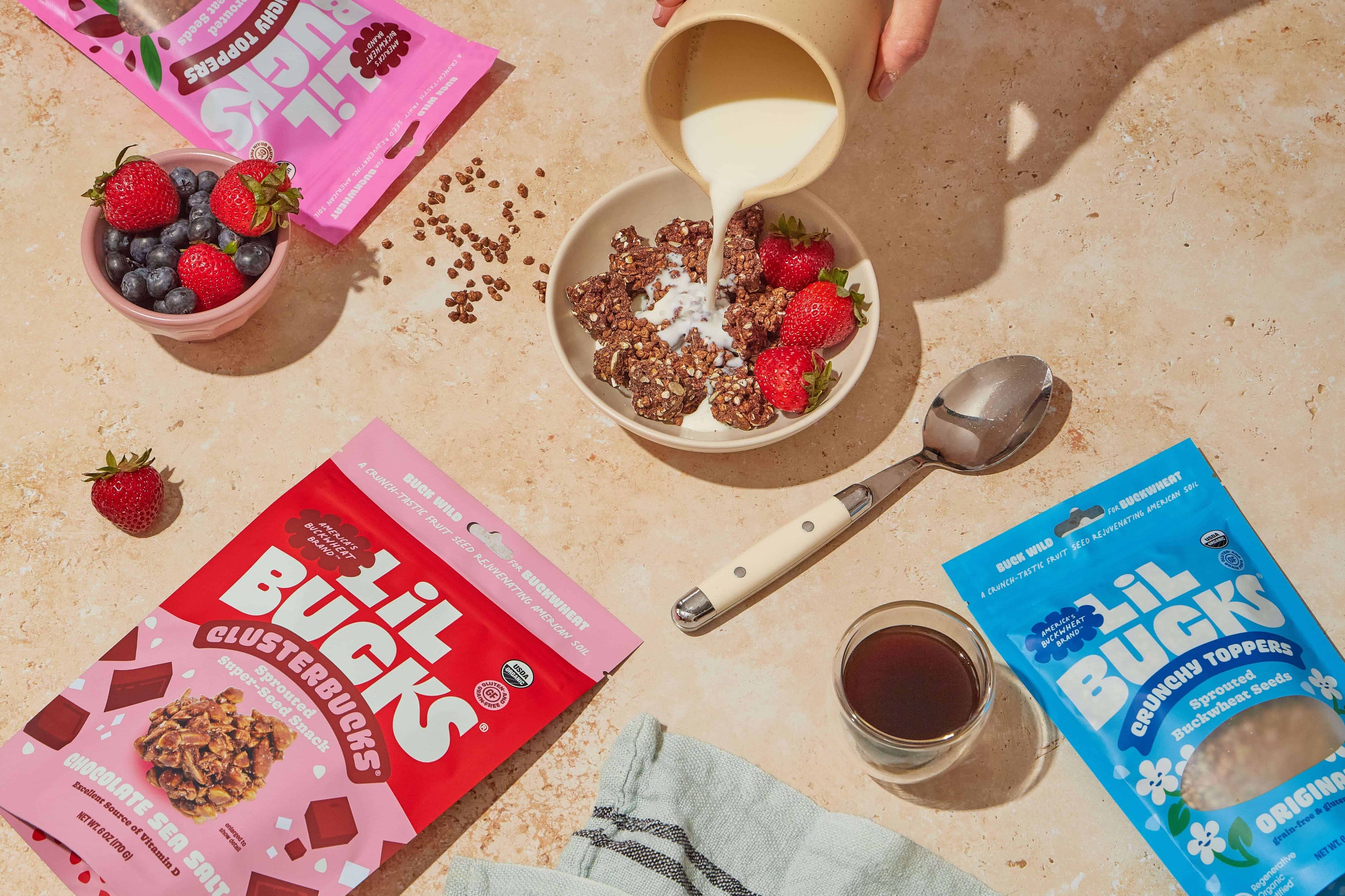 Person pouring milk into a bowl of cereal with berries, surrounded by 'Lil' Bucks' cereal packages on a tile surface.