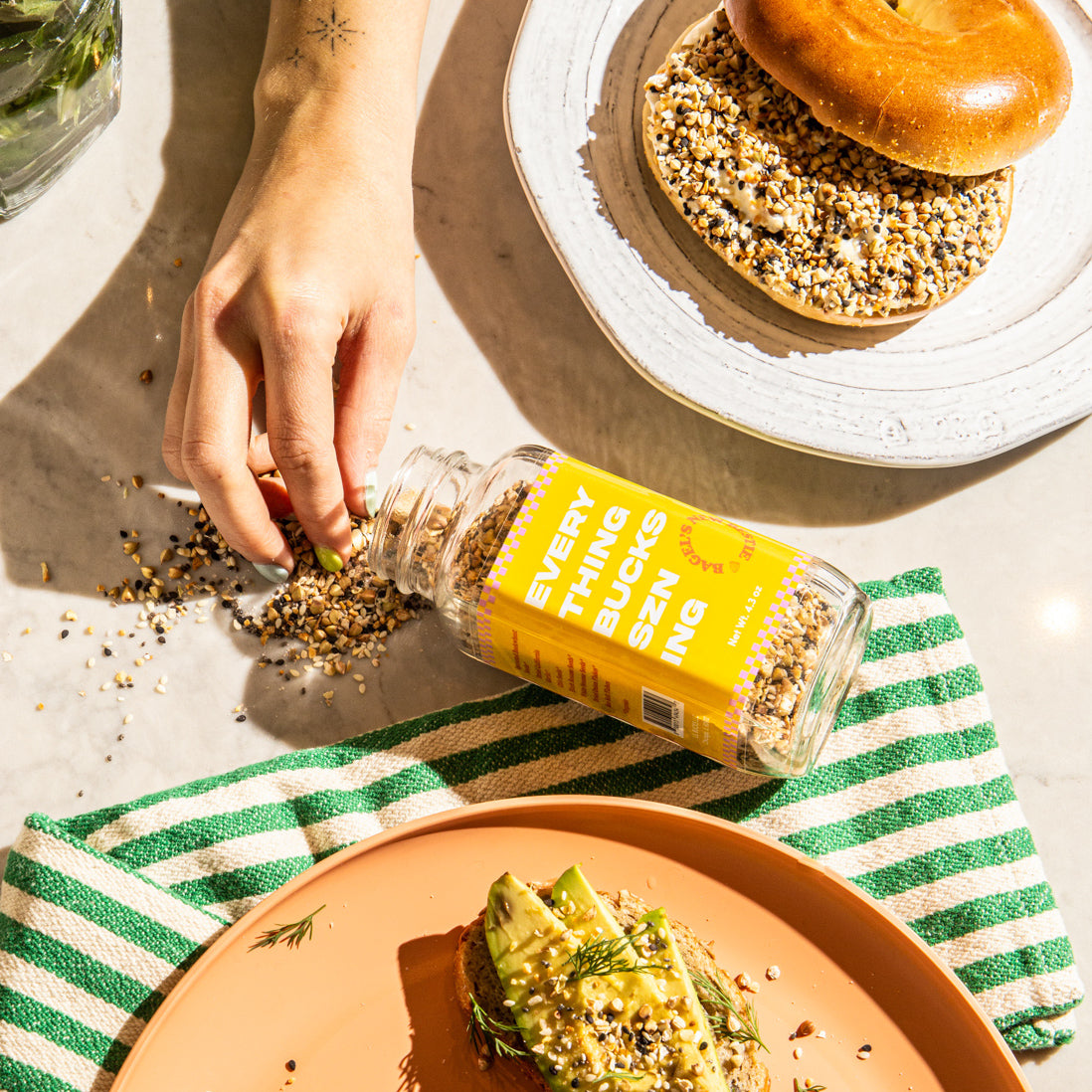 sprinkling avocado toast seasoning on bagel